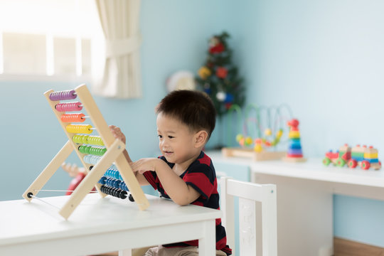Asian Toddler baby boy learns to count. Cute child playing with abacus toy. Little boy having fun indoors at home. Educational concept for Toddler baby.