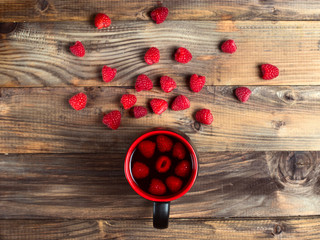 Tea with raspberries and berries next to a cup, on a wooden vintage table.