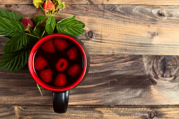 Tea with raspberries and berries next to a cup, on a wooden vintage table.