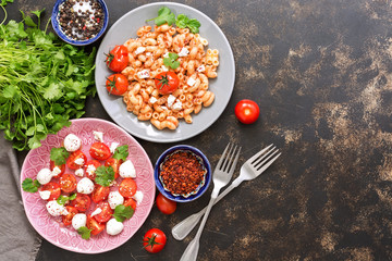 Italian dish of pasta with sauce and cheese. Salad with mozzarella and cherry tomatoes. Top view, space for your text.