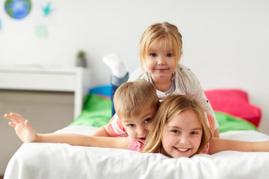 childhood, leisure and family concept - happy little kids having fun in bed at home