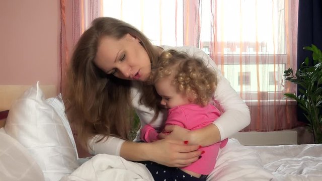 Mother calm down her little worried child girl by hugging embracing in bed