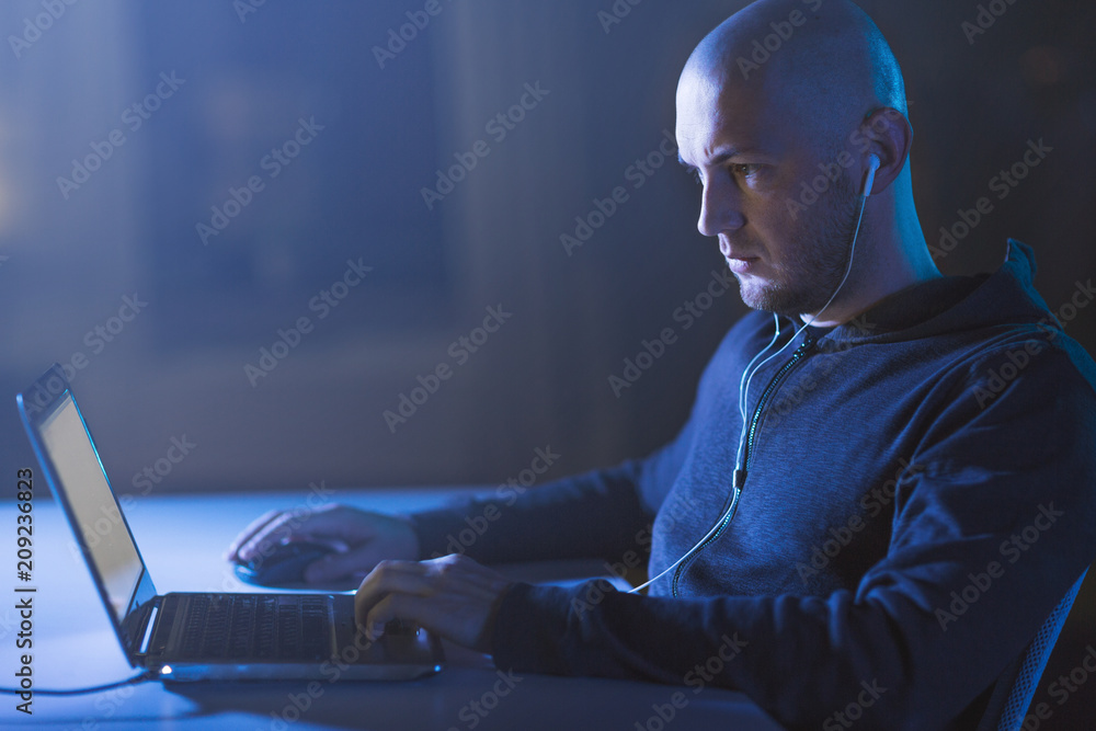 Poster cybercrime, hacking and technology concept - male hacker with earphones using laptop computer for cy