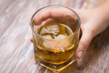 alcoholism, alcohol addiction and people concept - close up of male hand with glass of whiskey on table