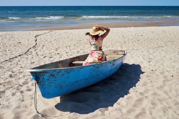 Girl with long dress and hat sitting in boat.