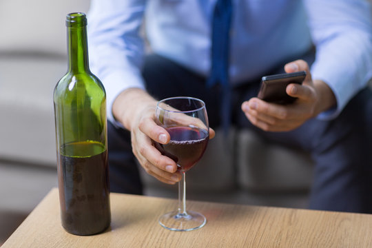 alcoholism, alcohol addiction and people concept - close up of man with glass of red wine, bottle and smartphone at home