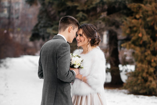 The bride and groom stand in the winter park, huddled together