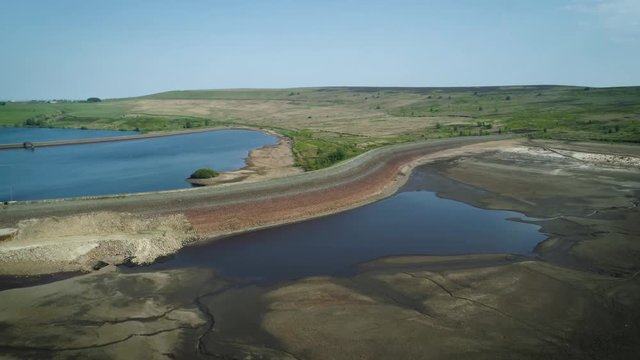 4K aerial drone shot of dried up reservoir on sunny day.