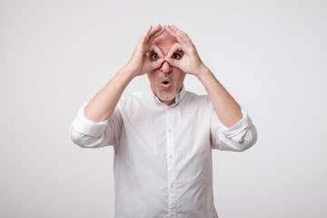 Mature caucasian man showing owl sign with fingers. Making funny grimace. Have a good mood