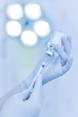 Hand holding syringe and medicine vial prepare for injection in operating room with surgery lamp background