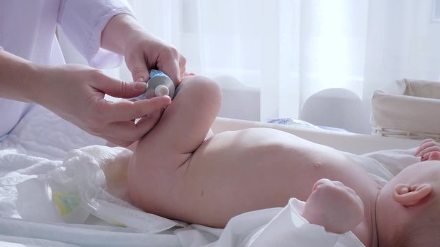baby care, Mother hands lubricate newborn skin with cream and change diaper in bright room close up