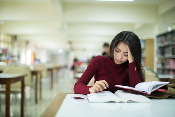 Tired young woman student of the University. Preparing exam and learning lessons in public library.