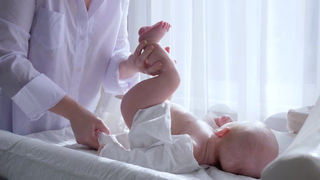 baby care, female changing diaper newborn lying on table at home against of curtains in natural light