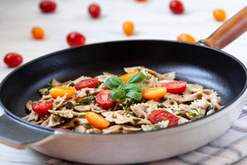 Whole-grained farfalle aglio olio with cherry tomatoes and fresh basil in a frying pan