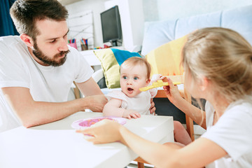 Good looking young man eating breakfast and feeding her baby girl at home