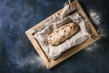 Christmas cake, traditional German festive baking. Wholegrain dough stollen preparation on linen napkin over dark blue texture background. Top view, space