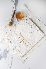 Homemade honey nuts nougat turron sliced on crumpled paper with lavender, glass of honey and sugar powder over white marble background. Flat lay, space.