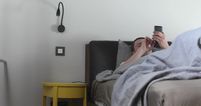 Man using mobile phone in bed AT HOME
