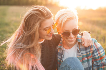 Two young women sitting on the field under light of sunset.