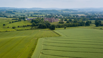 Aerial drone view of an ancient castle behind cultivated farmland and fields