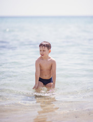 Adorable boy standing in the water on the beach. Family vacation or holiday concept.
