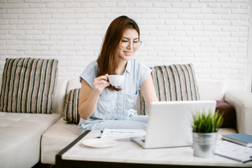 Young woman relaxing at home on the couch, she is having a coffee and using a laptop