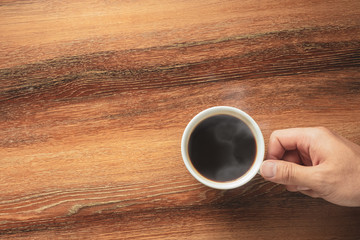 Hand of a man holding a hot black coffee cup on wooden table