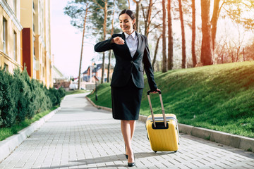 Beautiful young business woman in a suit and in shoes walking on a city street with yellow travel bag