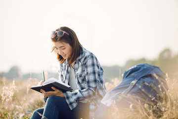 Beautiful young Asia woman writing on a journal about her hiking trip,flare light