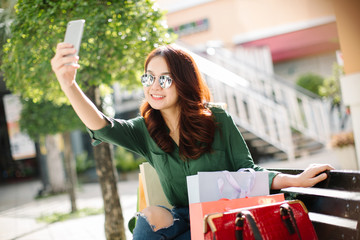 shopping Asia woman happy taking photo with smartphone. Woman holding shopping bags while taking...
