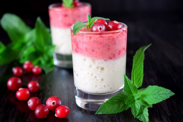 Two layered smoothie in glasses surrounded by cranberries and mint against the dark background