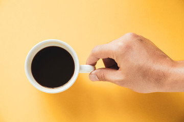 Hand of a man holding a hot black coffee cup on yellow background