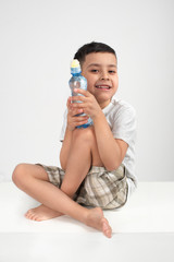  The little boy  of the brunette  wearing  grey shirt with small plastic bottle on a white background  in studio.