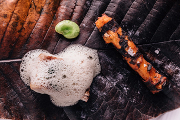 Creative Fine Dining: Fish topping with culinary foam serves with pea and grilled root with salt on torched leaf.