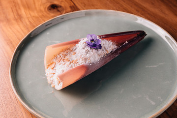 Creative Fine Dining Dessert: Touched banana topping with toffee cook by liquid nitrogen, looks like snow. Served in banana blossom peel and decorated with flower.