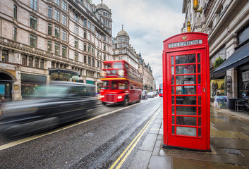 London, England - Iconic blurred black londoner taxi and vintage red double-decker bus on the move with traditional red telephone box in the center of London at daytime