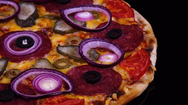 Colorful homemade pizza with pickles and onion just from oven rotating on black background in 4K. Closeup top view of traditional tasty food with free space for text from the right side.
