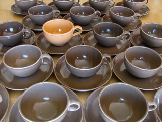 Stand out from the crowd. One unique orange cup is noticeable in a group of identical cups and saucers on a table.