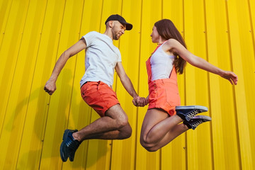 Happy couple in love jumping against yellow wall. Young hipsters