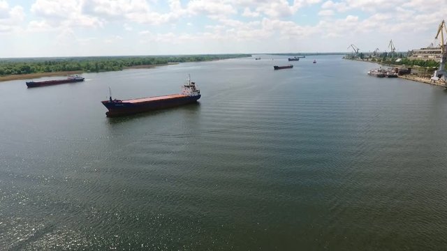 An exciting bird`s eye view of numerous cargo barges going slowly up the wide Dnipro river in summer. The port cranes are seen on the right.