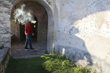 Obraz na płótnie Canvas Mann dreht sich um und wird vom Rauch einer Zigarette umhüllt, Schatten fällt auf eine Mauer