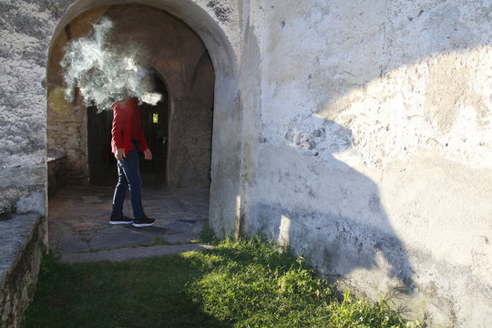 Mann dreht sich um und wird vom Rauch einer Zigarette umh&uuml;llt, Schatten f&auml;llt auf eine Mauer