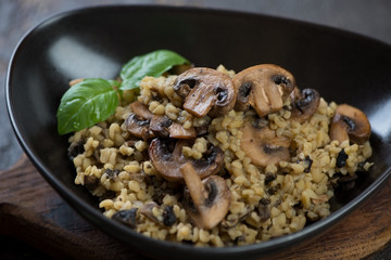 Close-up of bulgur wheat with slices of roasted champignons in a black bowl, selective focus, studio shot