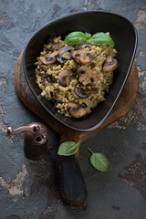 Bowl of bulgur with fried mushrooms on a rustic wooden serving board, vertical shot on a brown stone background