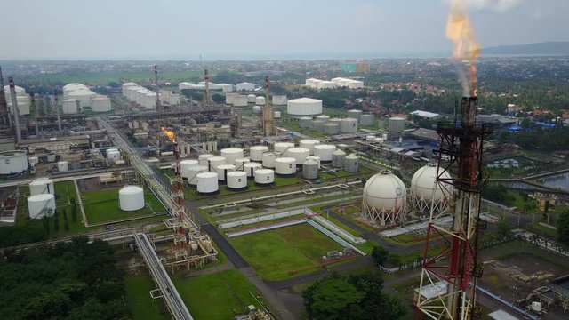 Flying past gas flare towards oil storage tanks of industrial facility in Indonesia
