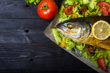 Baked sea fish with vegetables on a wooden table, free space.