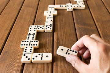 Playing dominoes on a wooden table. Man's hand with dominoes