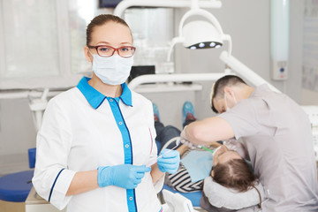 Portrait of female dentist with tools  in her dentist office and looking at camera. 
Medicine, stomatology, healthcare concept.  Doctor doing dental treatment on man's teeth in the dentists chair.