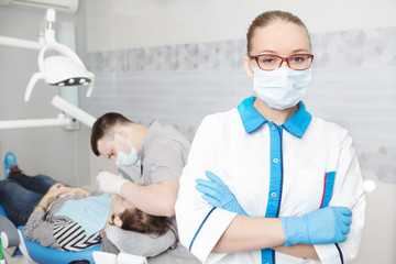 Portrait of female dentist with tools  in her dentist office and looking at camera. 
Medicine, stomatology, healthcare concept.  Doctor doing dental treatment on man's teeth in the dentists chair.