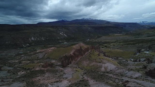 Los Bolillos red eroded rock formation on mountain slides of Varvarco valley. The Andes and varvarco river at background. Aerial drone scene descending slowly filming the formations